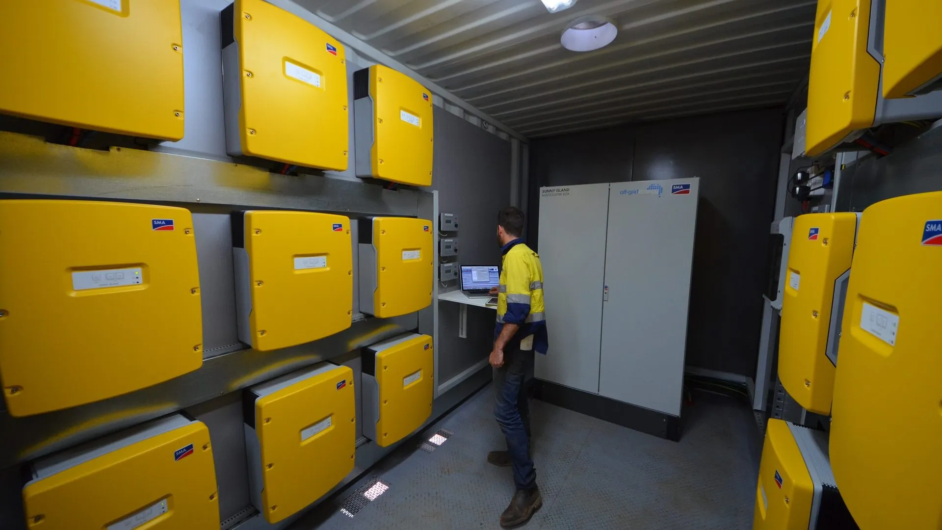 Technician beside SMA inverters in an off-grid plant room
